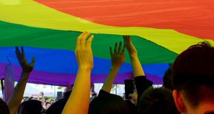 Photo of various hands holding up large rainbow flag