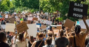 Crowd of people at a racial-justice protest; one sign reads, "Black Queer Proud"