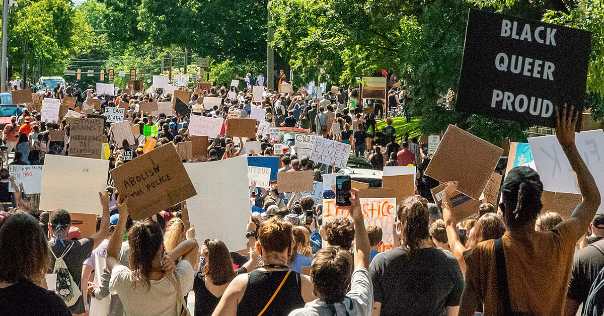 Crowd of people at a racial-justice protest; one sign reads, "Black Queer Proud"