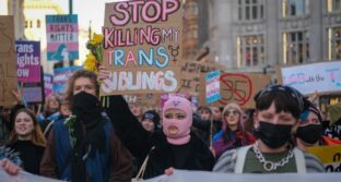 Protestors hold of signs such as "Stop killing my trans siblings" and "LGB with the T"