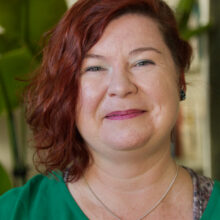 A smiling woman wears a green shirt. She is Caucasian, has red hair.